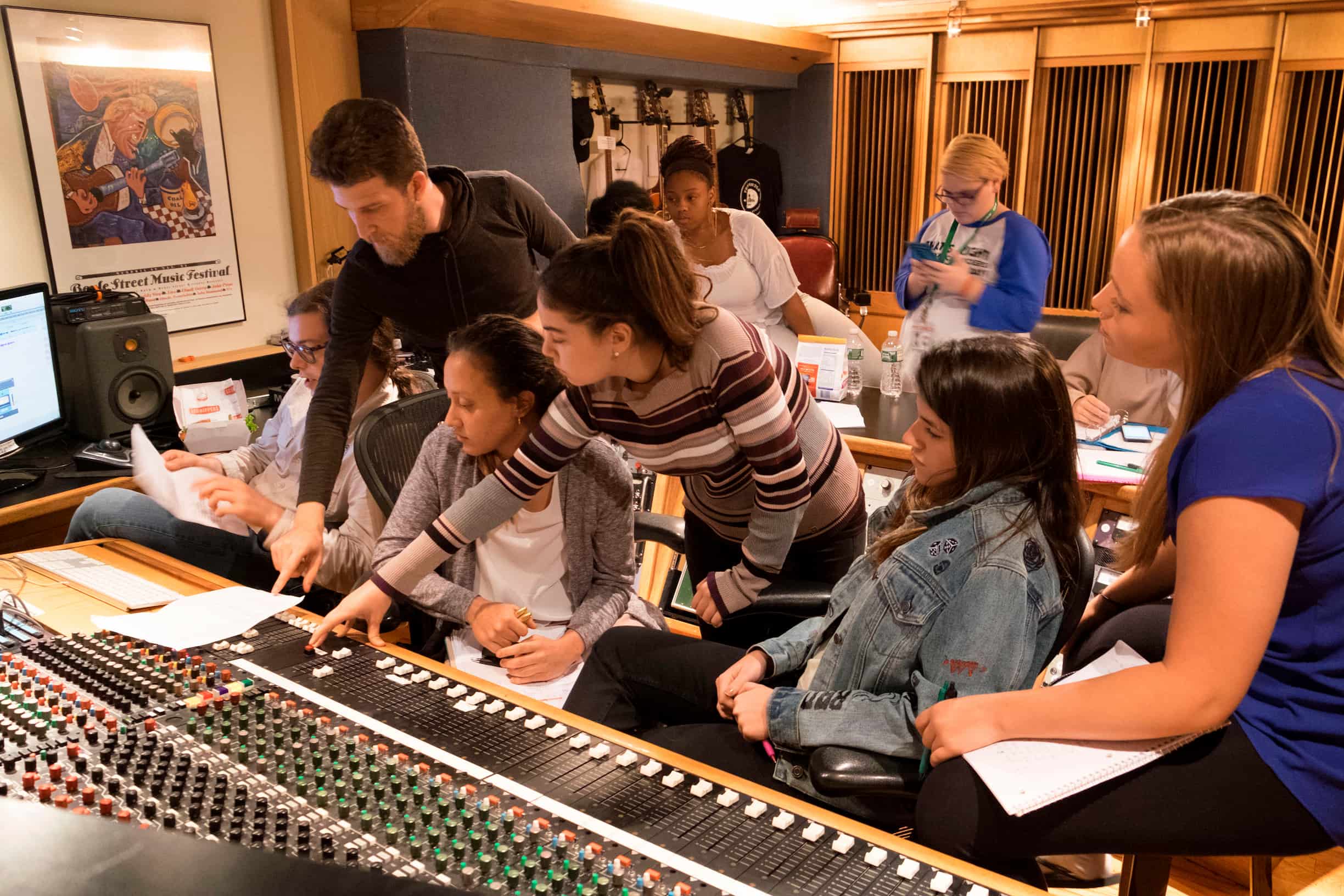
	Three students in a professional recording studio, wearing headphones and working on music production.